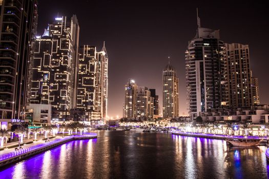 Illuminated skyscrapers reflecting in Dubai Marina at night. Captivating urban skyline scene.