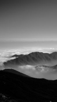 Black and white breathtaking view of rough rocky mountains peaks surrounded with thick clouds