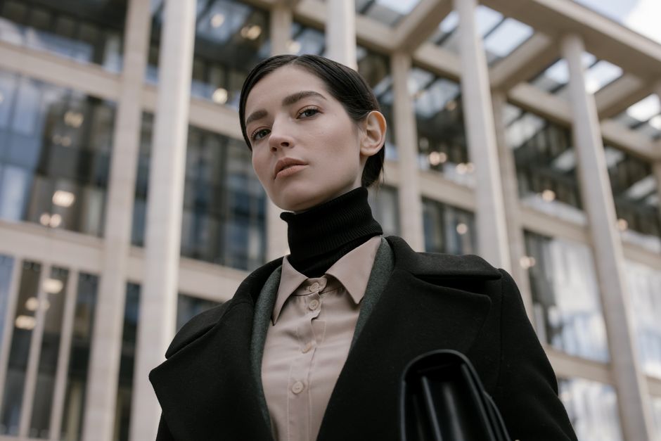 A fashionable young woman in professional attire with urban architecture background.