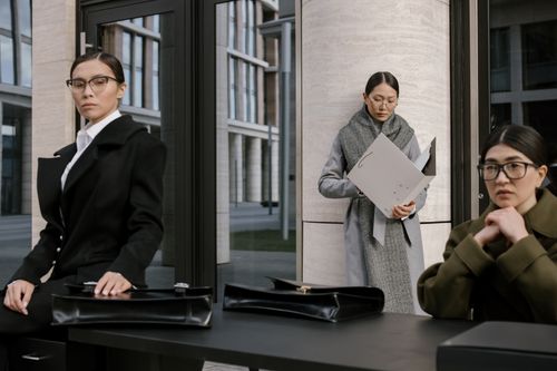 Free Three professional women in formal outfits with briefcases, posing outside a modern office building. Stock Photo