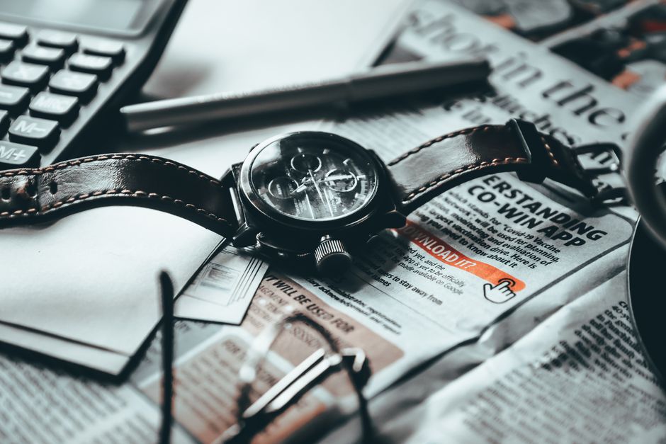 High angle of wristwatch placed on newspaper next to papers with calculator near pen and eyeglasses on table in light room High angle of wristwatch placed on newspaper next to papers with calculator near pen and eyeglasses on table in light room