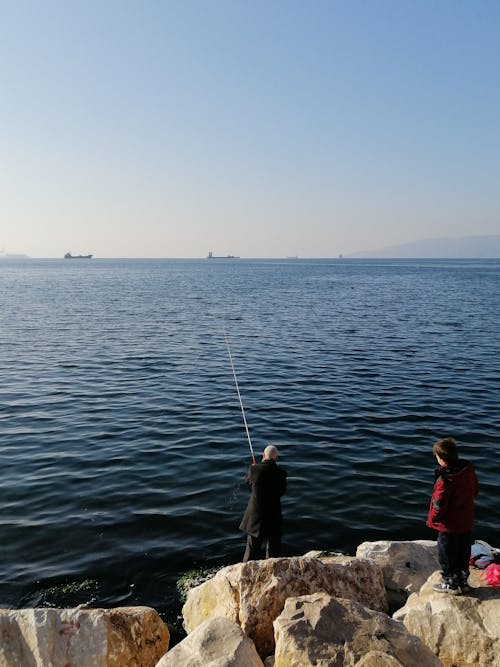 A Boy Watching a Man Catching Fish in the Sea