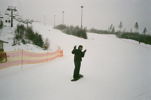 Full body anonymous snowboarder in warm clothes standing on snowboard on snowy mountain slope and showing two fingers gesture while spending weekend in ski resort