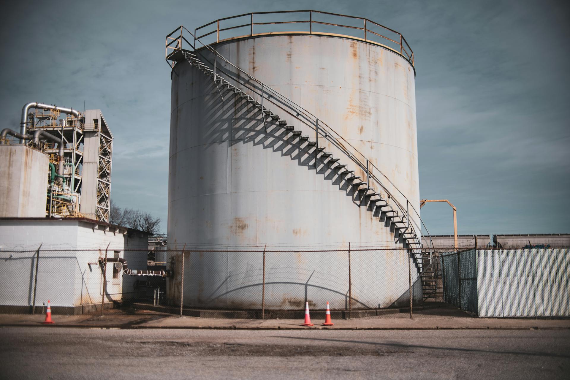 Industrial storage tank with metal stairs in an outdoor facility under clear sky.