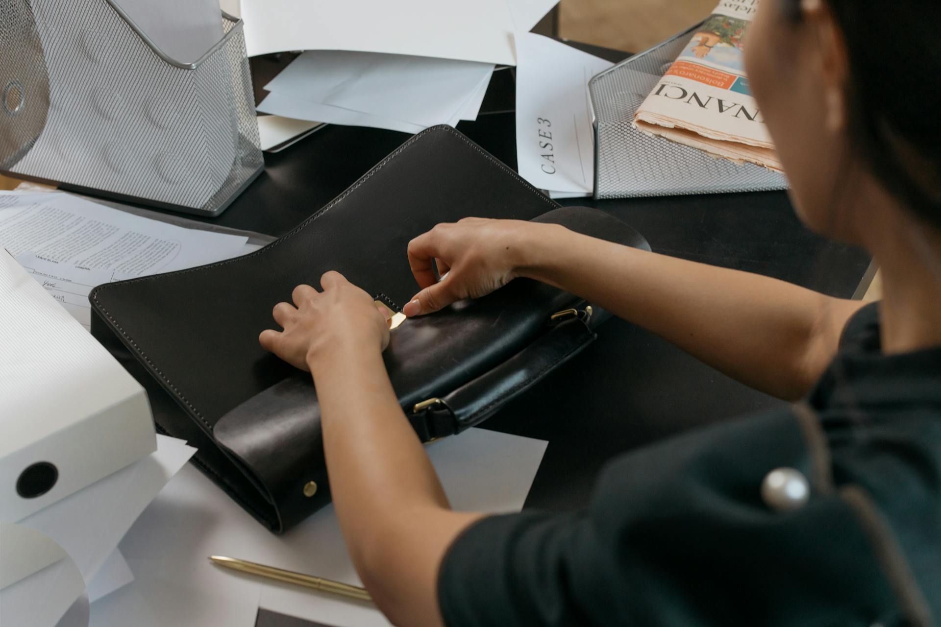 A professional organizing paperwork at an office desk with a leather briefcase.