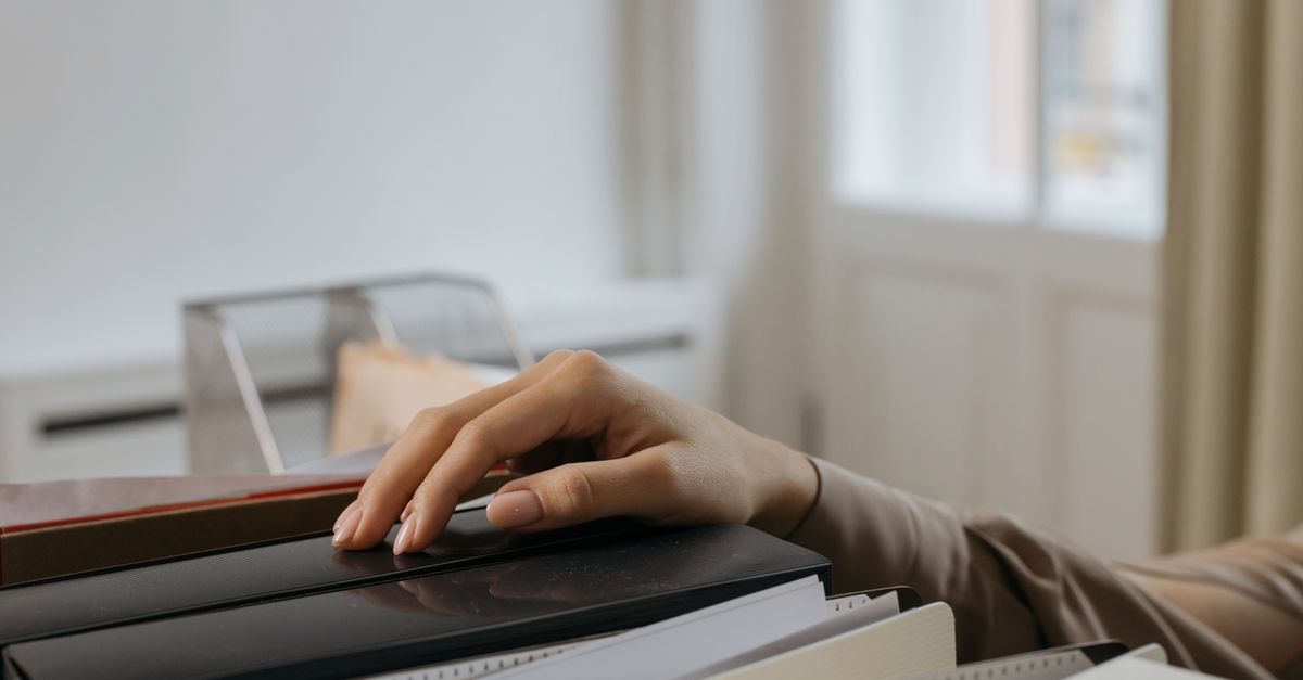 An adult's hand reaches for office file folders, capturing a thoughtful moment. Indoors setting.