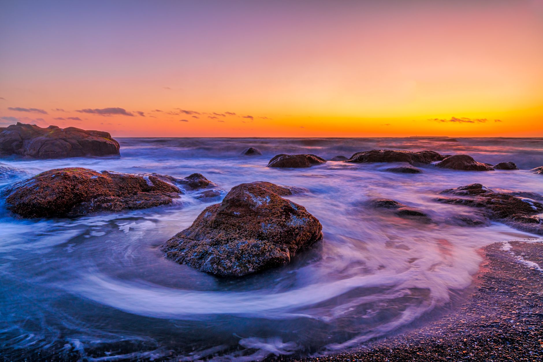 Vibrant sunset over a rocky seashore in Forks, WA with waves crashing dramatically.