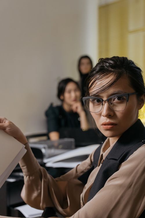 Free Young Asian woman in glasses working with colleagues in a modern office setting. Stock Photo