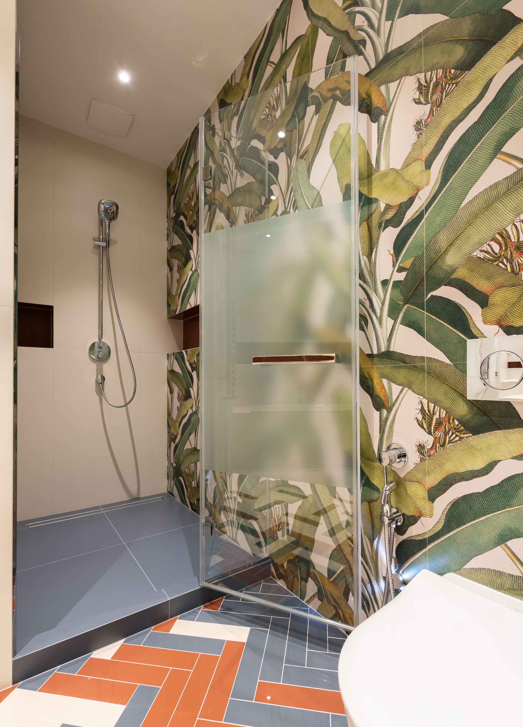 Modern bathroom with full-height tropical leaf wallpaper, a clear glass shower and colorful geometric floor tile