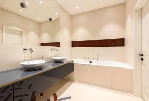 Interior of contemporary minimalist styled bathroom with ceramic sinks and big mirror near bathtub