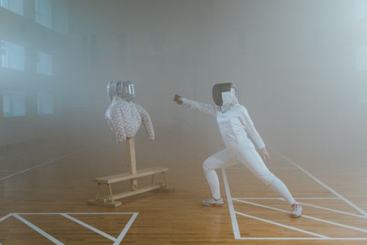 Woman practicing fencing indoors with a dummy target, showcasing sportsmanship and skill.
