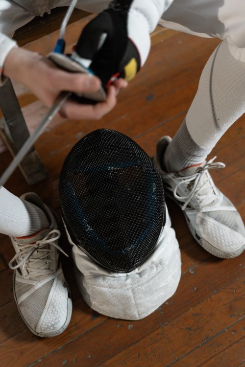 Free Detailed view of a fencer preparing gear indoors, focusing on fencing mask and footwear. Stock Photo