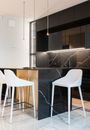 Interior of contemporary kitchen with white chairs at island counter in kitchen with black cabinets in modern apartment