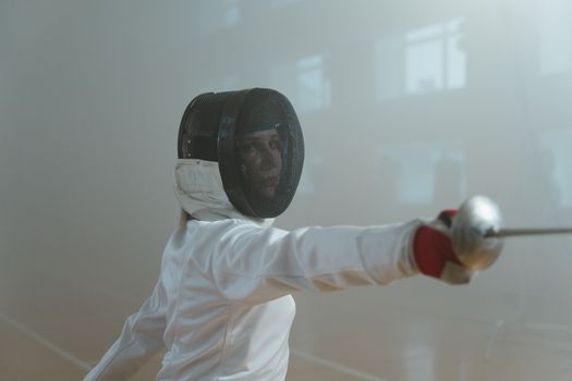 A female fencer skillfully thrusting her sword in a fencing arena. Indoor sports.