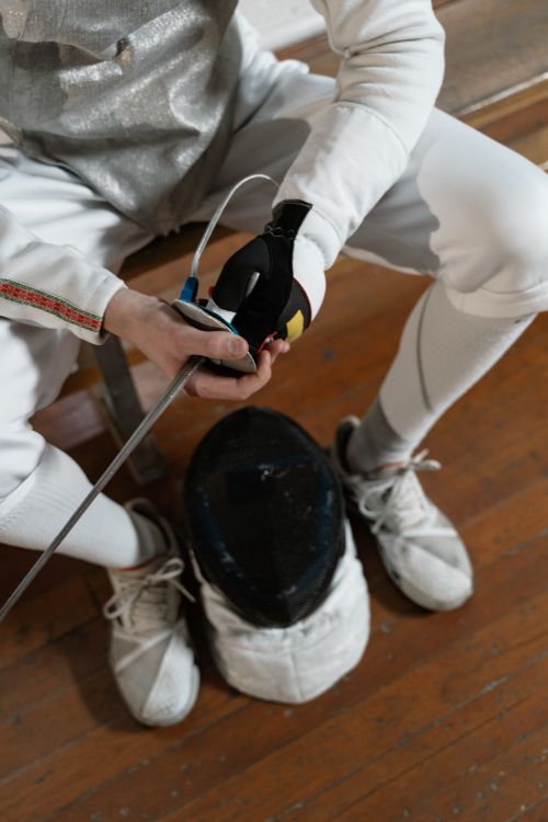 Free A fencer sitting indoors, holding a sword, preparing for a match. Focus on equipment. Stock Photo