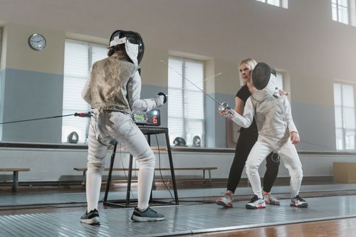 Free Two fencers practicing under the guidance of a coach in a sports hall. Stock Photo