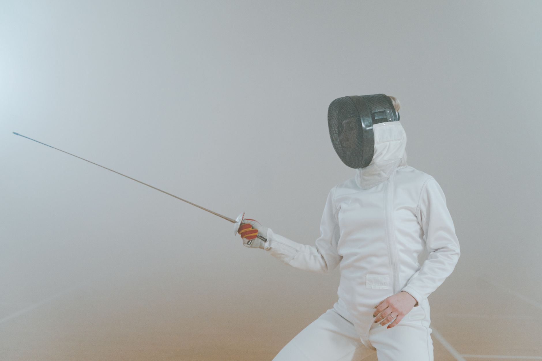 A female athlete in fencing gear striking an en garde pose in a foggy setting.