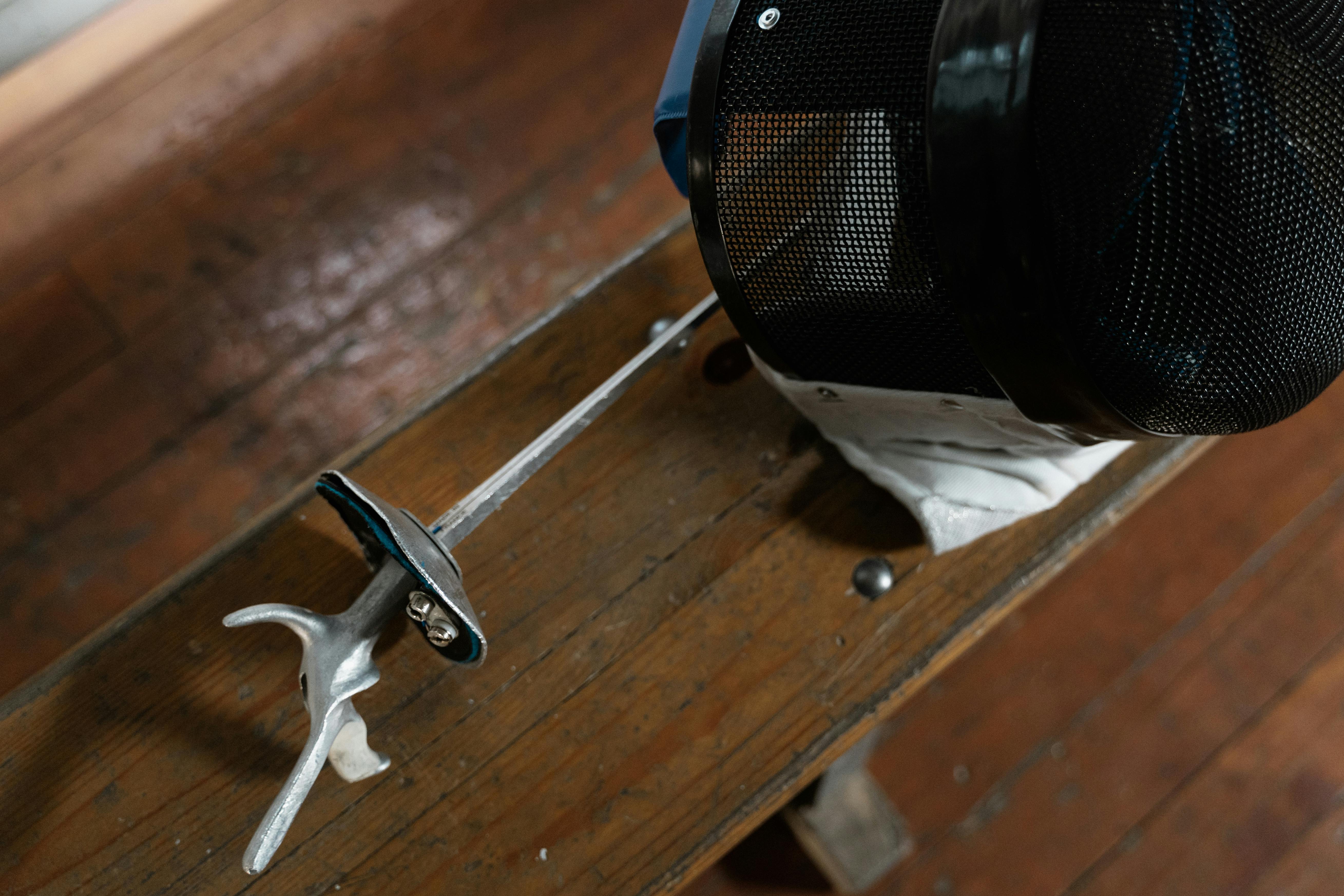 a fencer mask and sword over a wooden bench