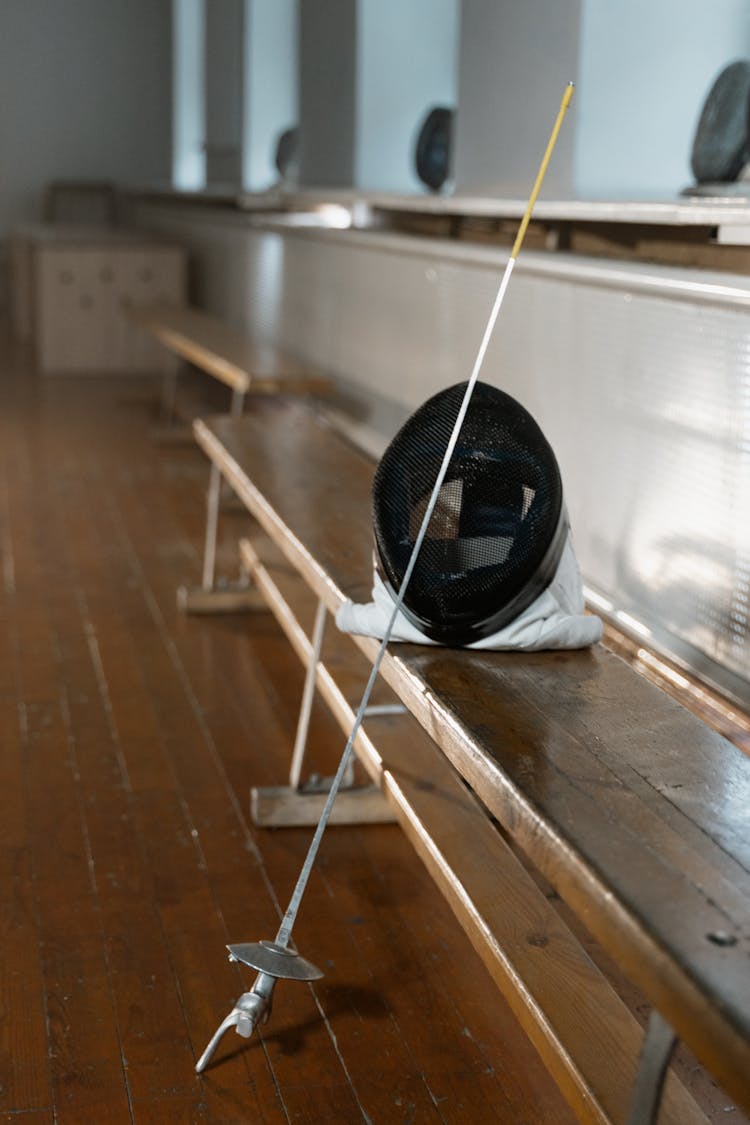 An Epee And A Mask On A Wooden Bench