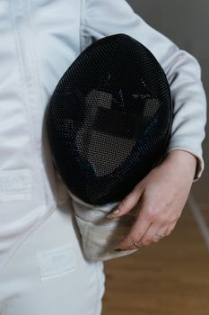 Close-up of a fencer holding a protective mask, showcasing gear and safety equipment.