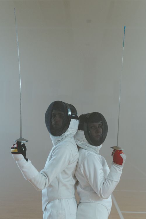 Free Two fencers in full gear posing back to back, showcasing swords and masks, ready for a match. Stock Photo