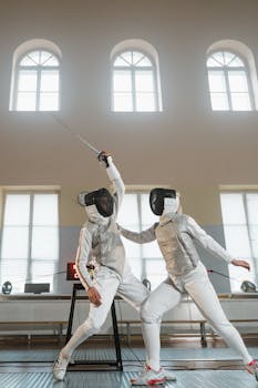 Two athletes engaged in a thrilling fencing match indoors, showcasing skillful dueling techniques.
