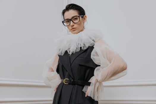 Chic woman in a stylish outfit with eyeglasses posing gracefully indoors.