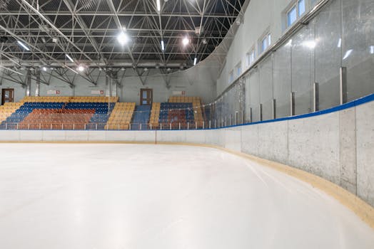 An empty indoor ice skating rink with colorful seating and bright lighting, ideal for sports events.