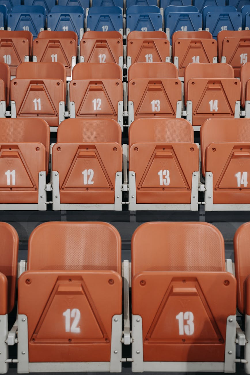 Close-up of orange and blue numbered stadium seats in vertical rows.