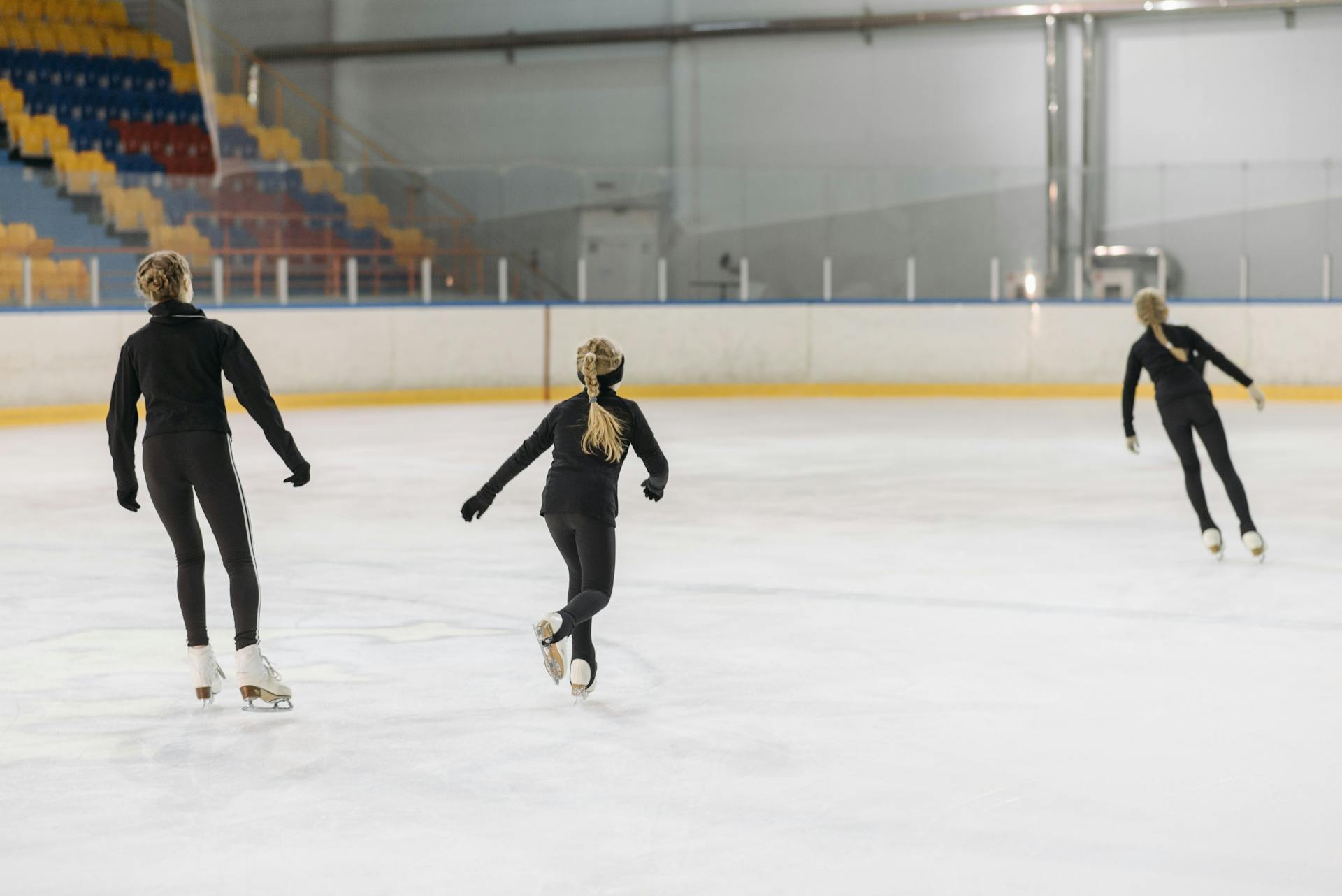 Three young figure skaters practicing on an indoor ice rink.