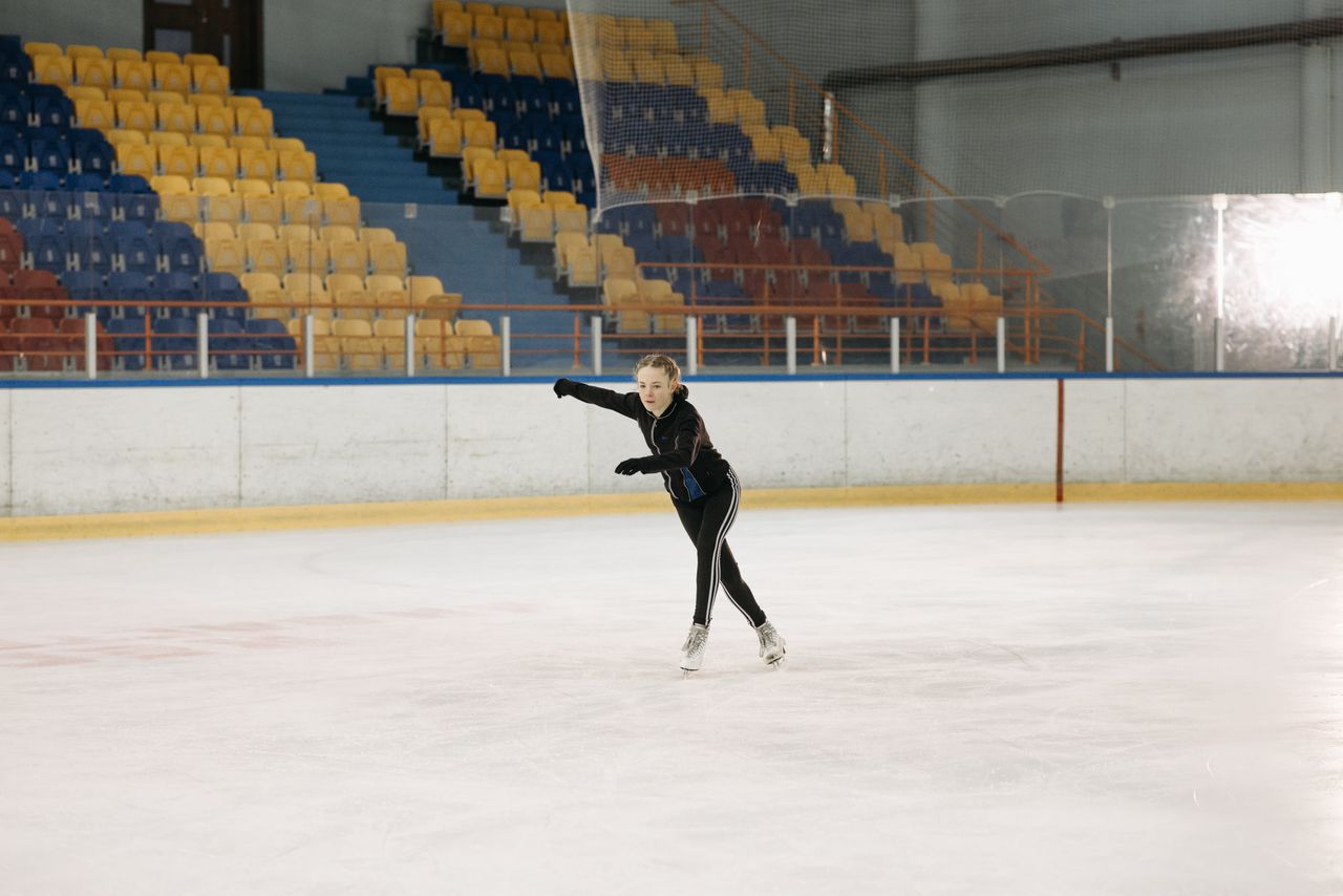 a young woman elegantly figure skating on an indoor ice rink showcasin