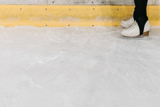 Close up of ice skater's feet wearing skates against a yellow rink barrier.