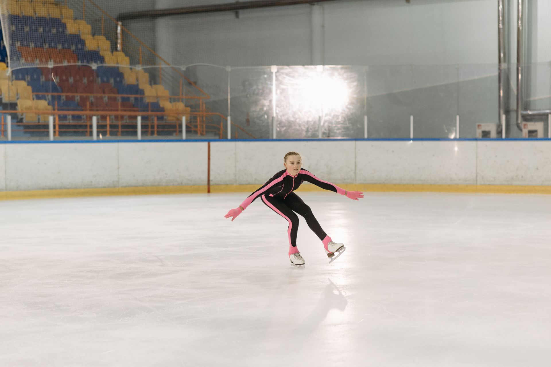 A young girl in a black and pink outfit skates gracefully on an indoor ice rink.