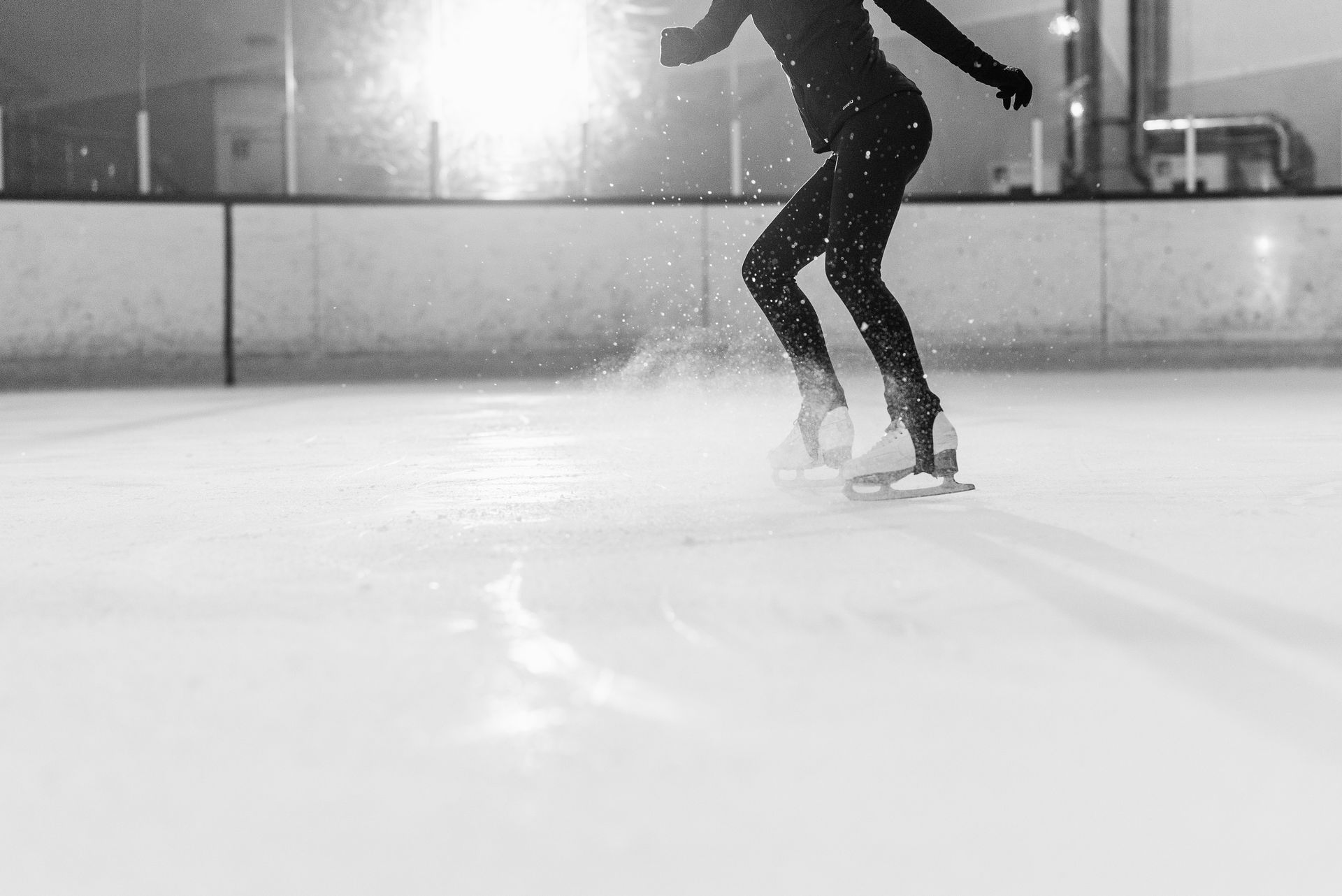 Black and white photo of a figure skater gliding on an indoor ice rink, creating a dramatic scene.