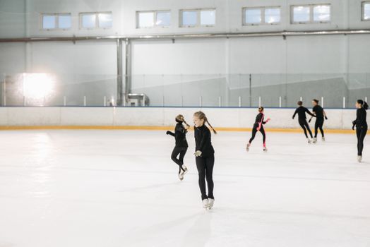 A group of young figure skaters practicing indoors on an ice rink, honing their skills.