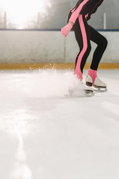 Ice skater in motion on indoor rink in winter attire, creating spray of ice.