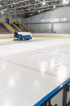 Zamboni machine cleaning an empty indoor ice skating rink with colorful seats.