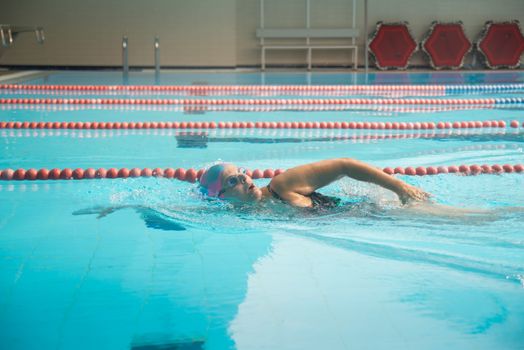 Adult female swimmer practicing freestyle stroke in a bright indoor swimming pool setting.
