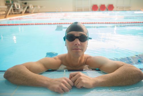 Free Adult male swimmer wearing goggles and cap relaxing at the edge of an indoor pool. Stock Photo