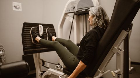 Mature woman working out on a leg press machine in a gym, promoting active and healthy lifestyle.