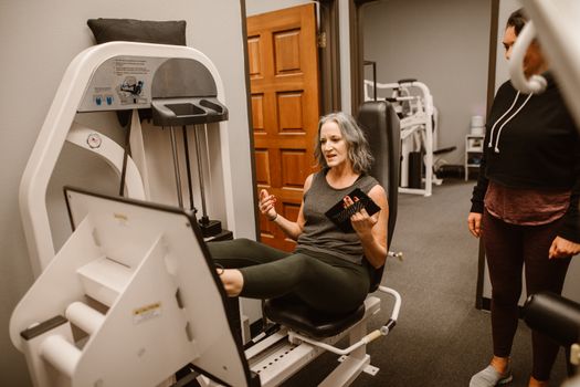 Senior woman working out on a leg press machine with a trainer at a gym.