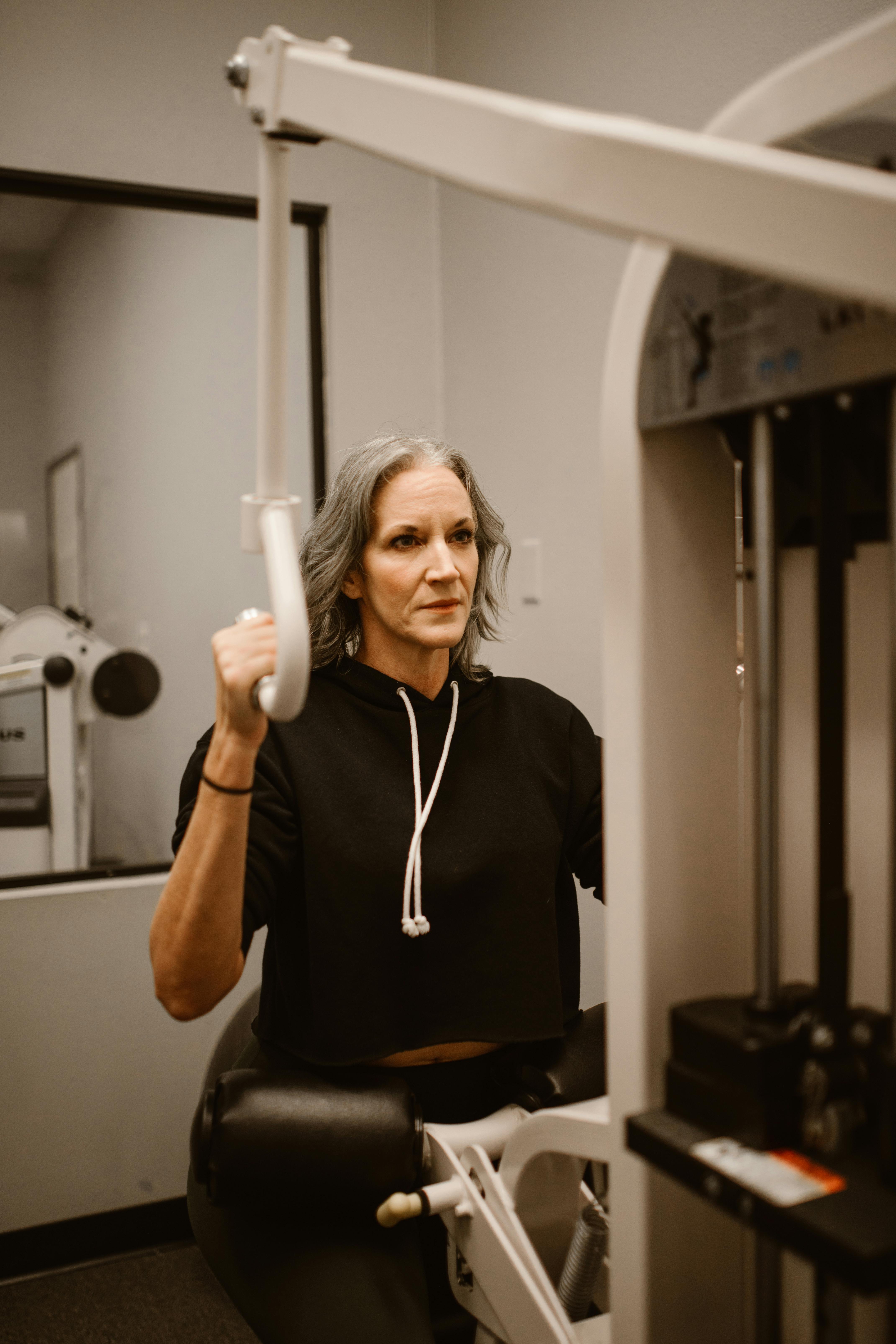 A senior woman focused on workout using a gym machine indoors, promoting fitness and health.