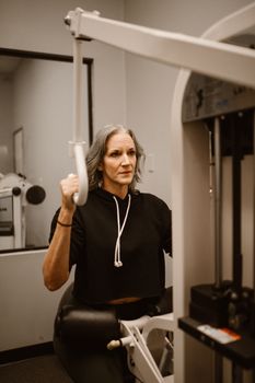 A senior woman focused on workout using a gym machine indoors, promoting fitness and health.