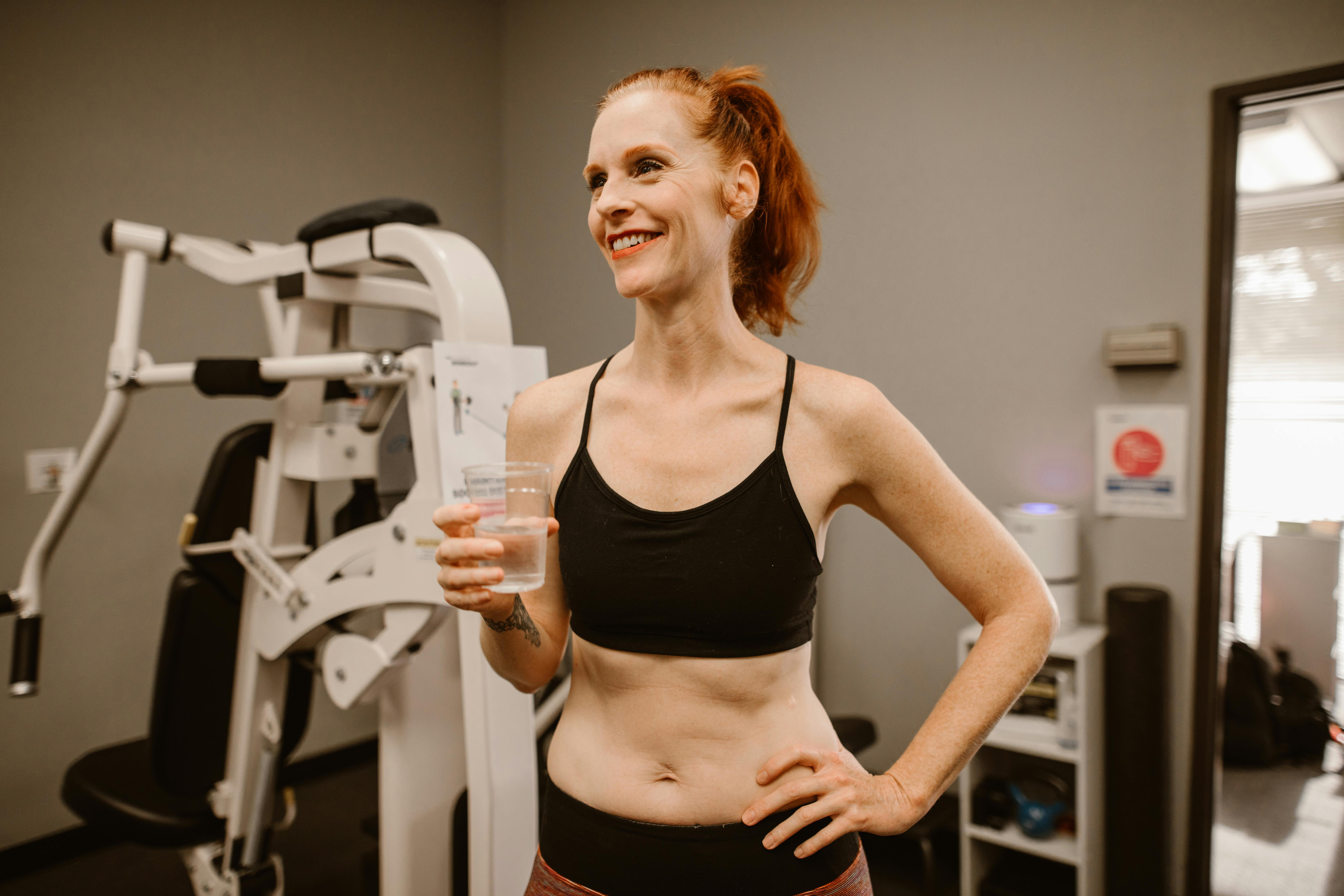 Caucasian woman smiling, holding water, and enjoying a healthy lifestyle at the gym.