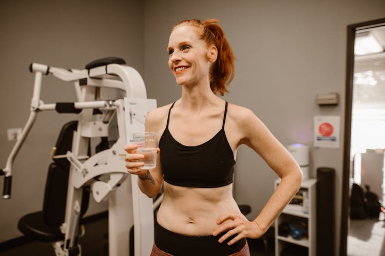 A Happy Woman Holding A Glass Of Water At A Gym