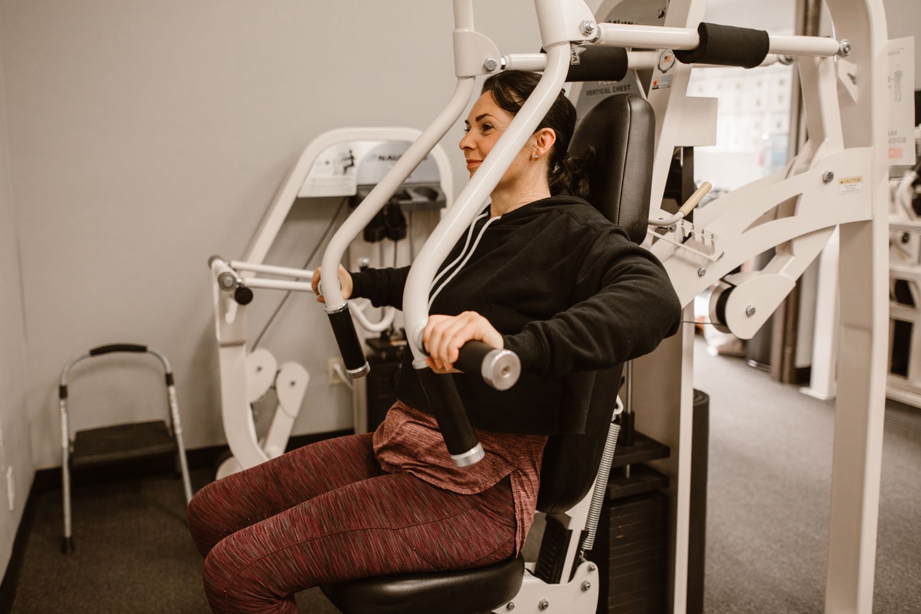 weight loss post-vaccine women over 40 — Woman working out on a chest press machine, promoting fitness and health in a gym setting.