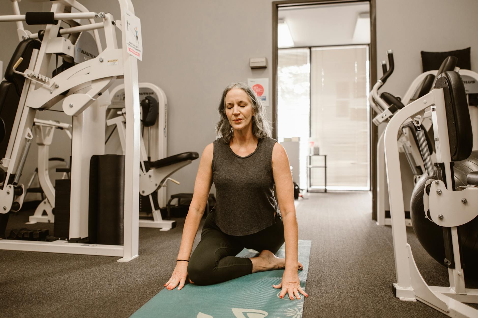 A midlife woman meditates on a yoga mat in a gym, practicing mindfulness and wellness.
