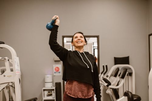 Free Smiling woman lifting a kettlebell in a gym setting, showcasing fitness and well-being. Stock Photo