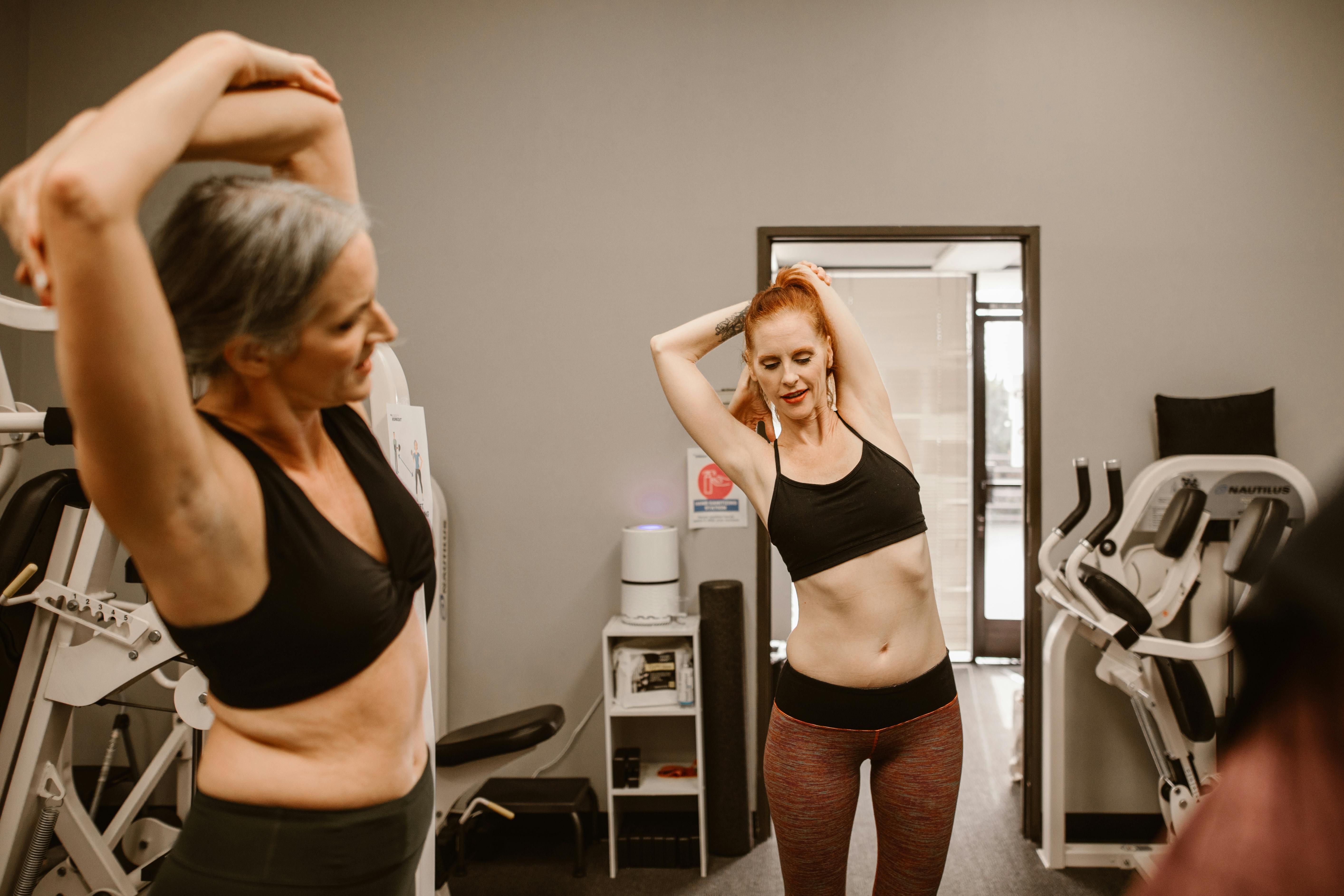 Two women stretching in a gym, preparing for a fitness routine. Active lifestyle concept.