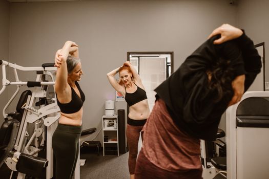 Three women stretching at the gym, promoting fitness and healthy lifestyles.